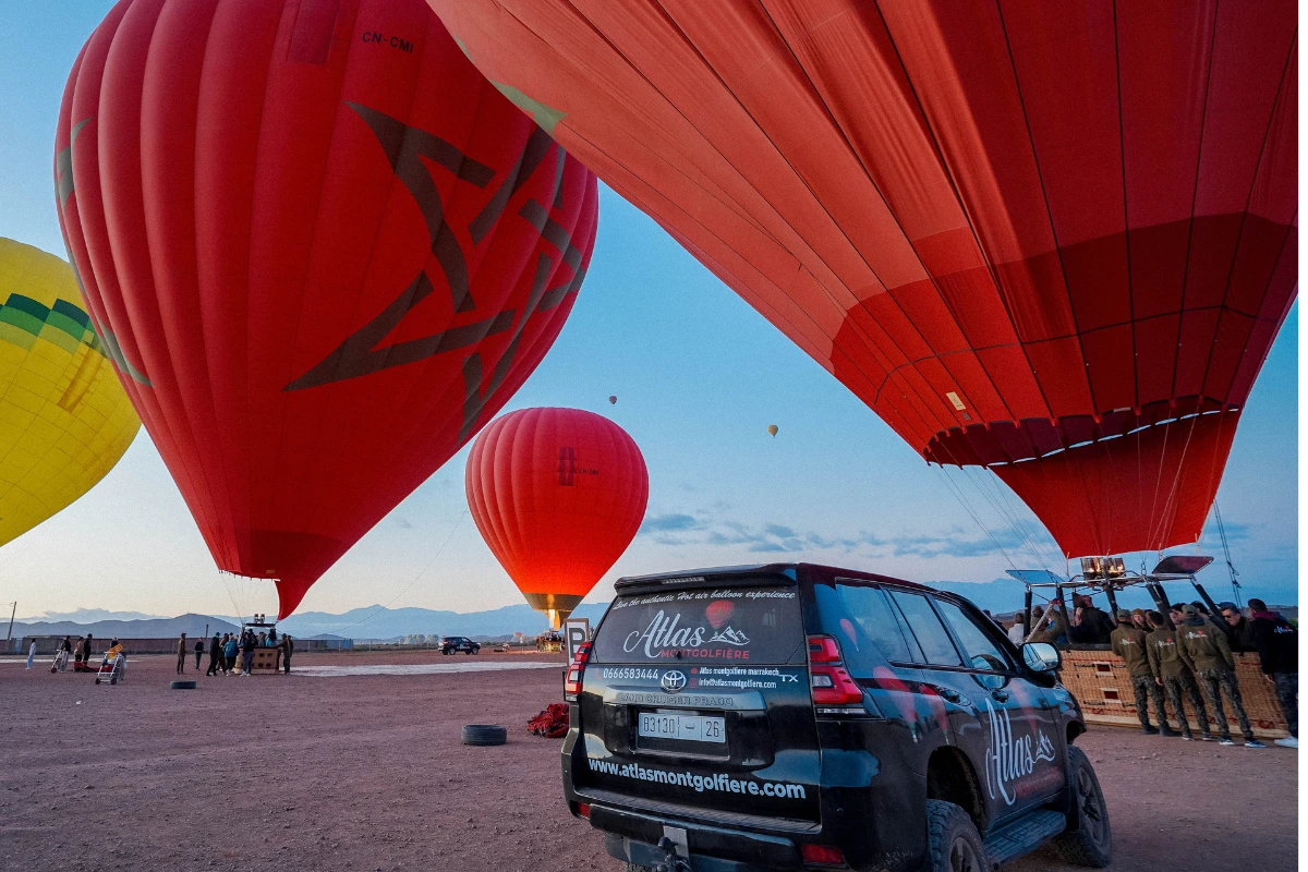 Préparation d’un vol en montgolfière Marrakech au lever du soleil avec véhicules de transfert Atlas Montgolfière et montgolfières prêtes au décollage.