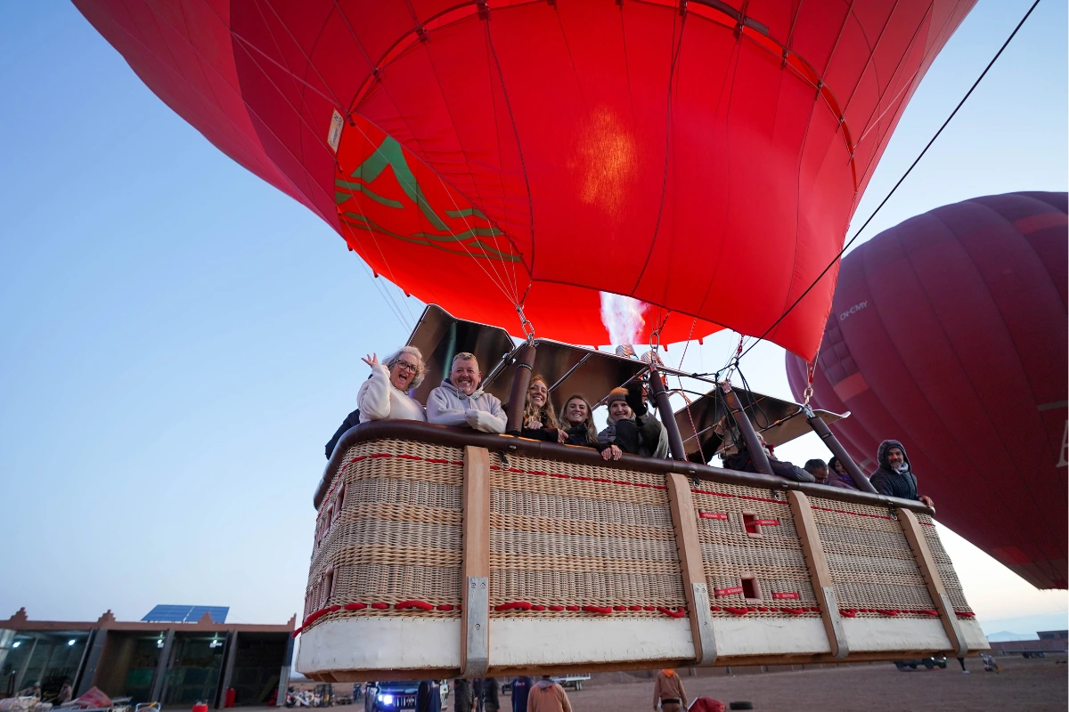 Touriste souriante prenant une photo lors d’un vol en montgolfière à Marrakech au lever du soleil.