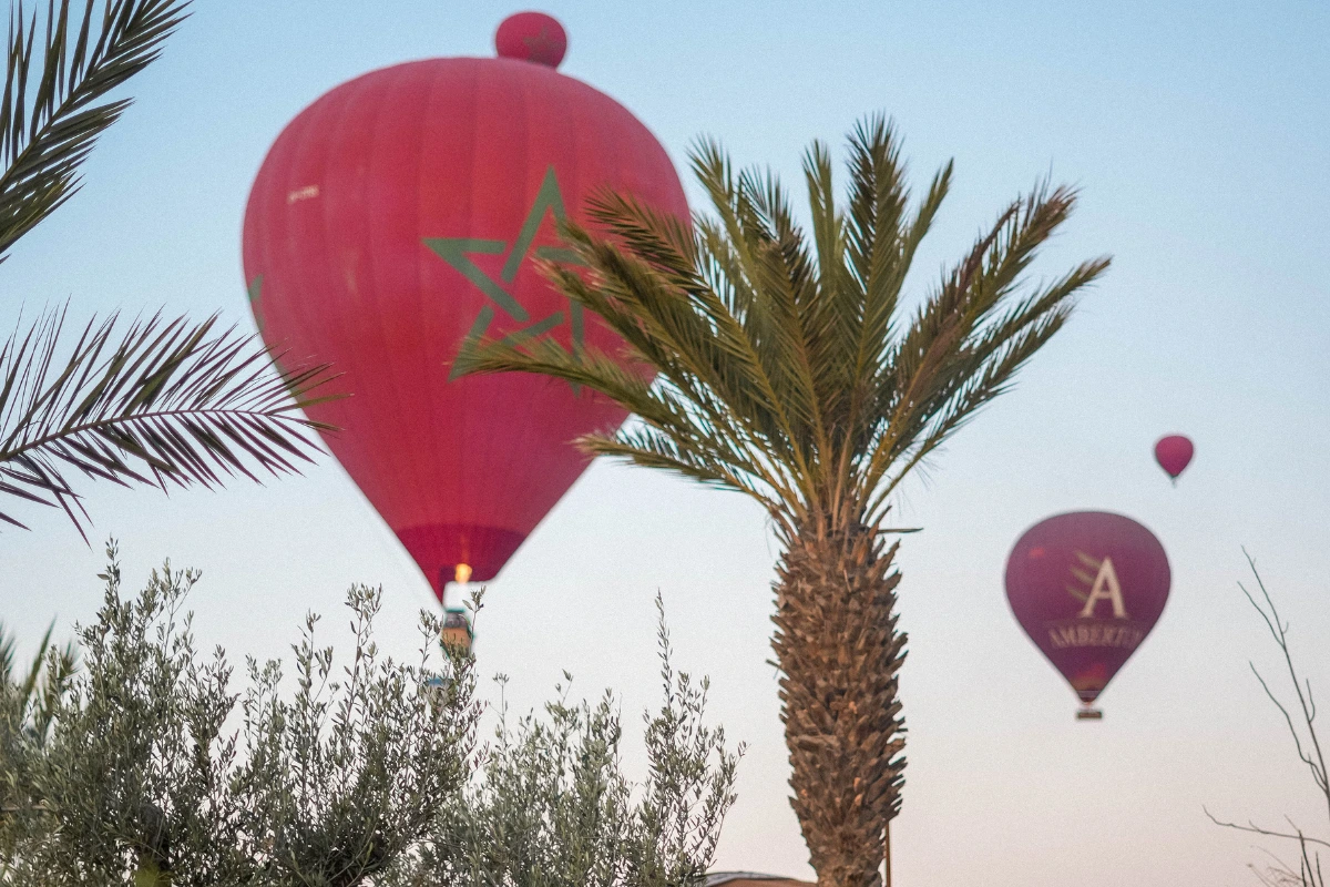 Vol en montgolfière Marrakech au lever du jour, avec des ballons rouges survolant les palmiers et les paysages marocains.